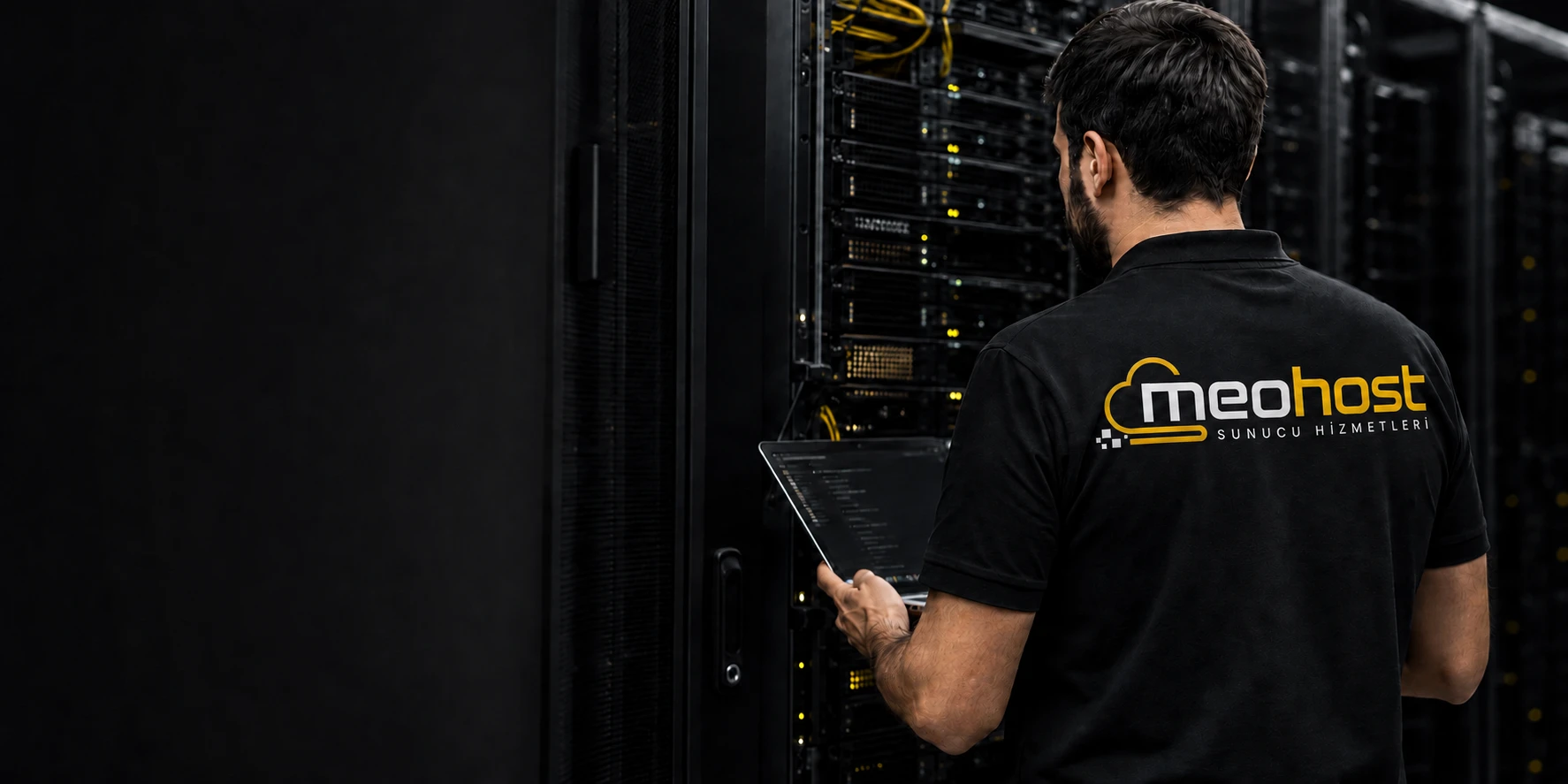 Sırtında MeoHost baskılı siyah polo ile veri merkezinde çalışan teknik uzman
